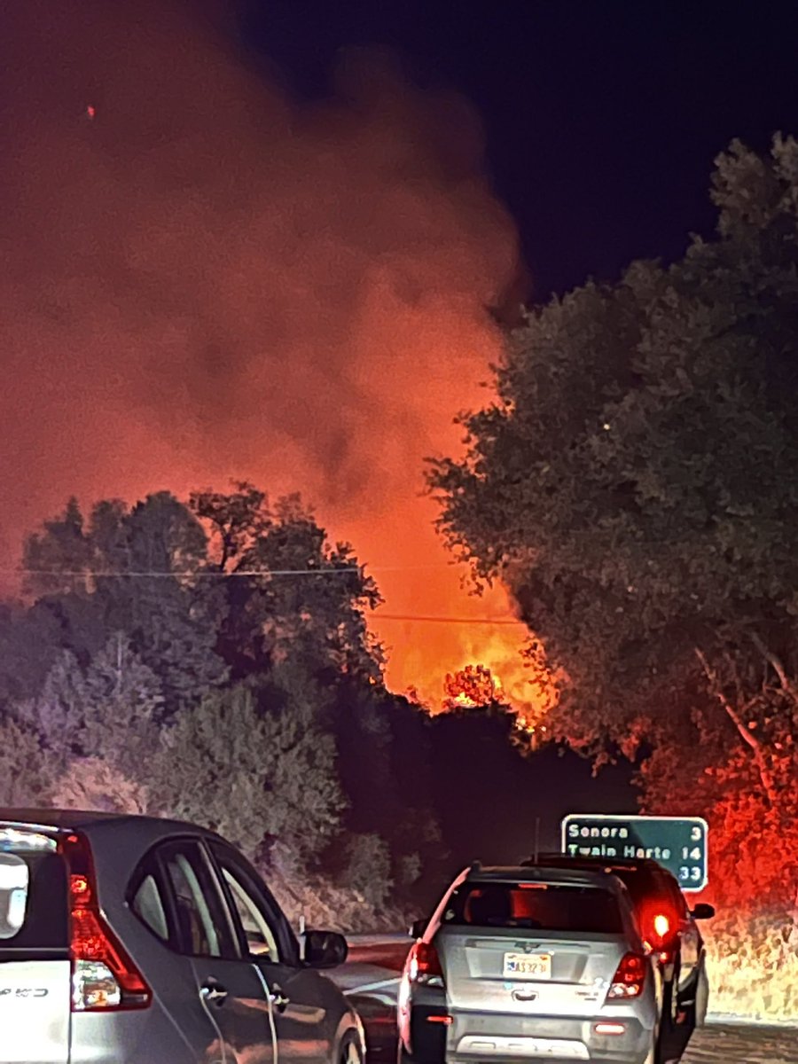 Looking toward the WoodsFire from Jamestown, 3 miles away from Sonora. We just arrived at this spot moments ago. We can see  flames, bright orange glow in the night sky. Evacuees/people stopped on the side of Hwy 49 looking fire